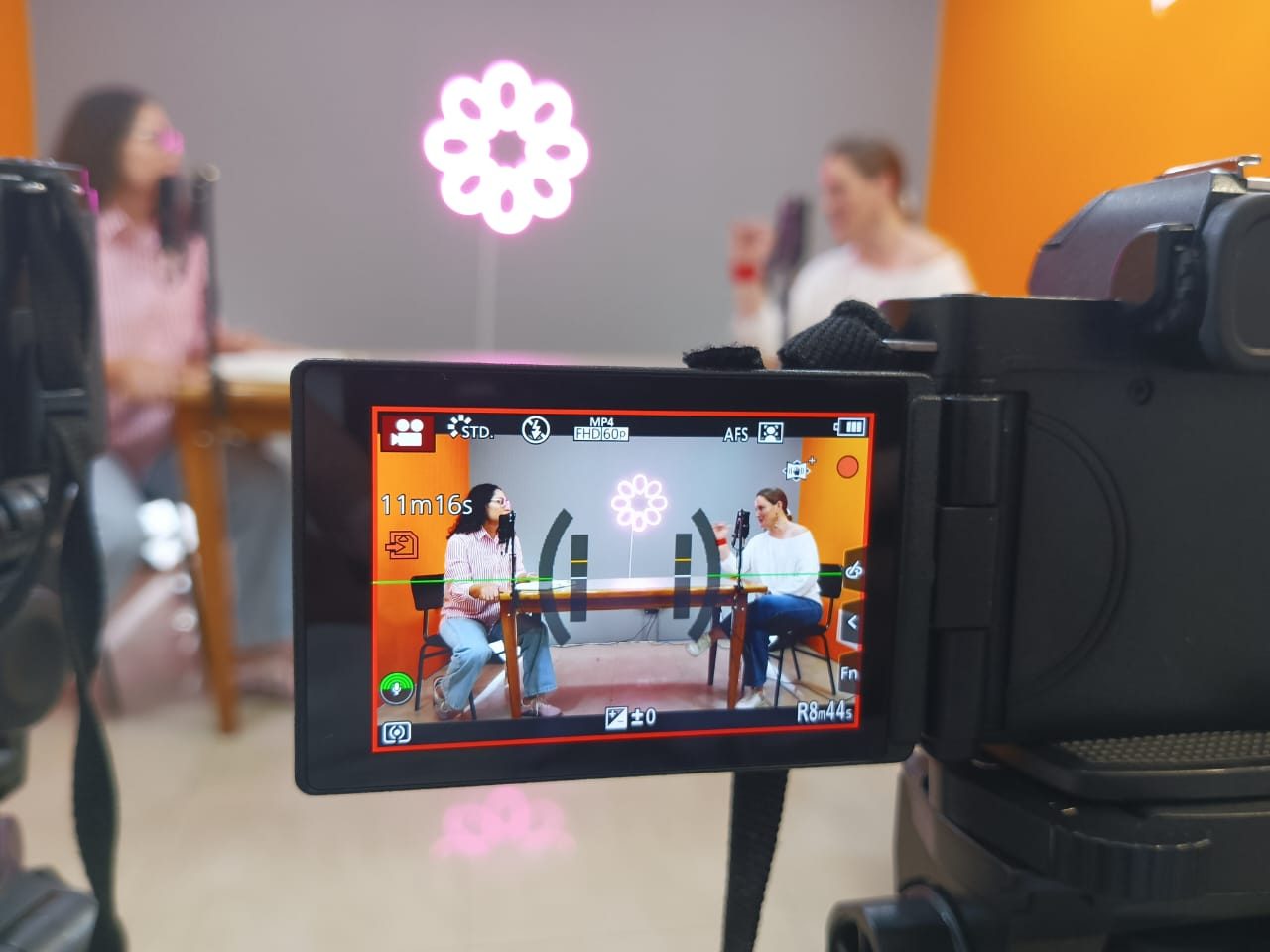 Monitor de cámara que encuadra a dos participantes conversando en el set del podcast